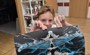 Chłopczyk pokazuje prace na ciemnym papierze