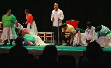 Kuba stoi i wygłasza kwestie, aktorzy leżą na ziemi