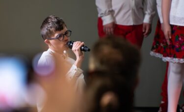 Chłopczyk mówi do mikrofonu. W tle publiczność.