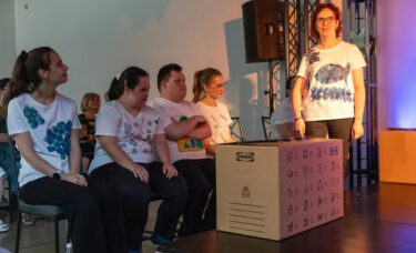 Grupa aktorów siedzi i patrzy jak Karolina deklamuje swoją kwestie.